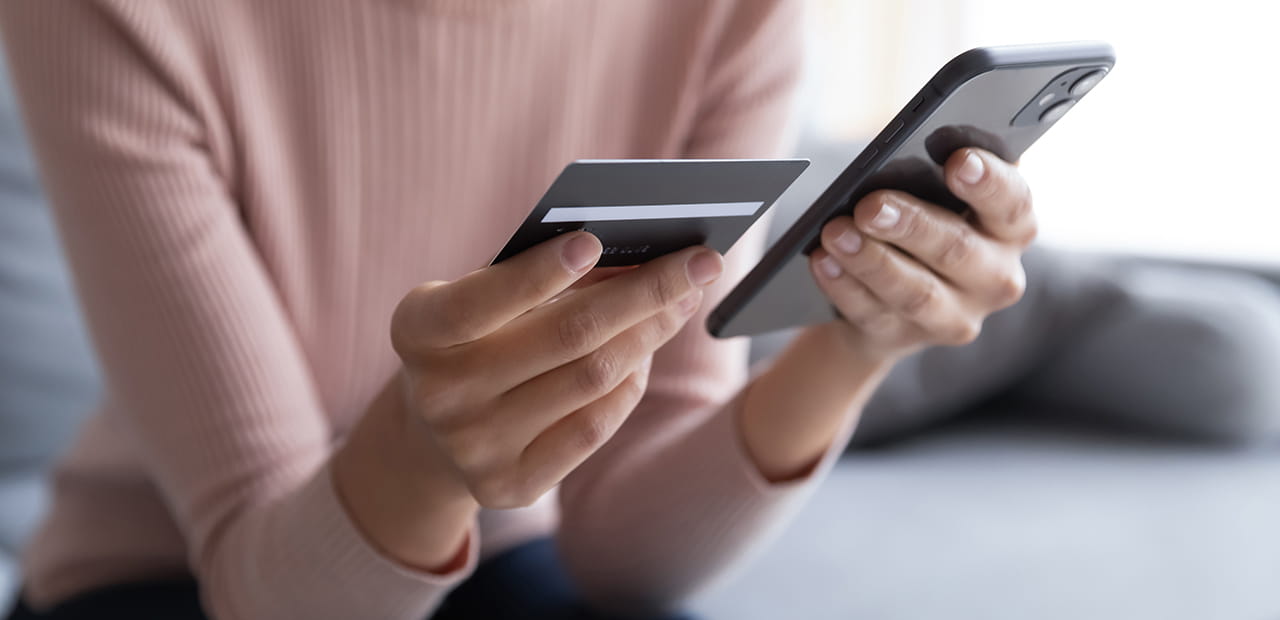A woman holding a credit card in one hand and a cell phone in the other