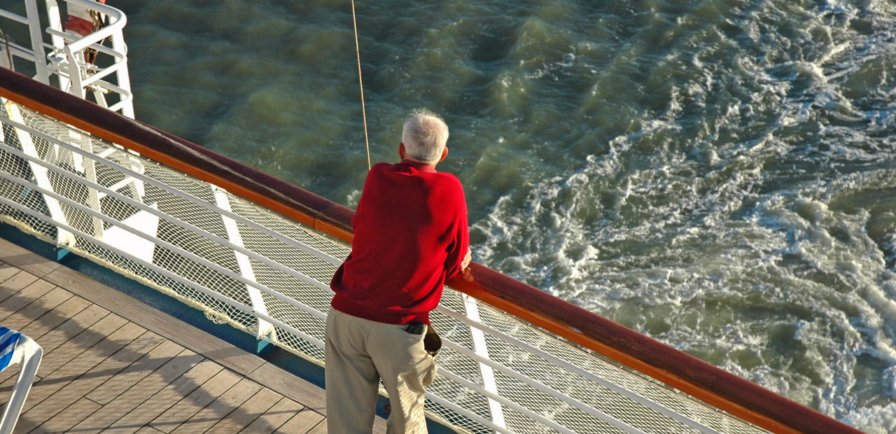A senior man looks out over the rail of a cruise ship.